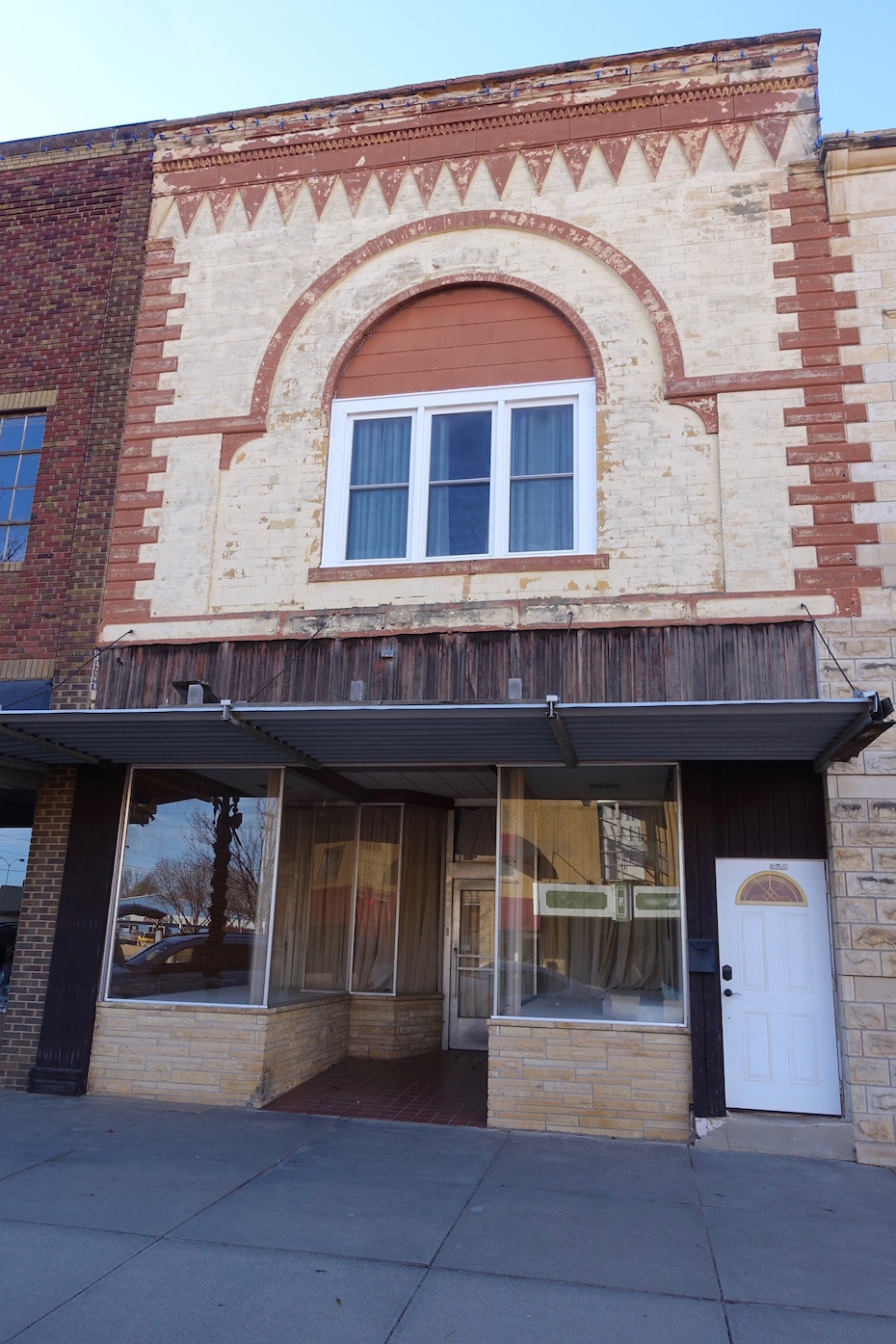 The building, which likely dates to the late 1870's, features some very beautiful stone work on the facade. The present windows are recent replacements which fail to make use of the spectacular arched opening. The door to the stairwell has been replaced with another stylistically inappropriate choice. It relates to neither the Italianate second story nor the 1950's entry.